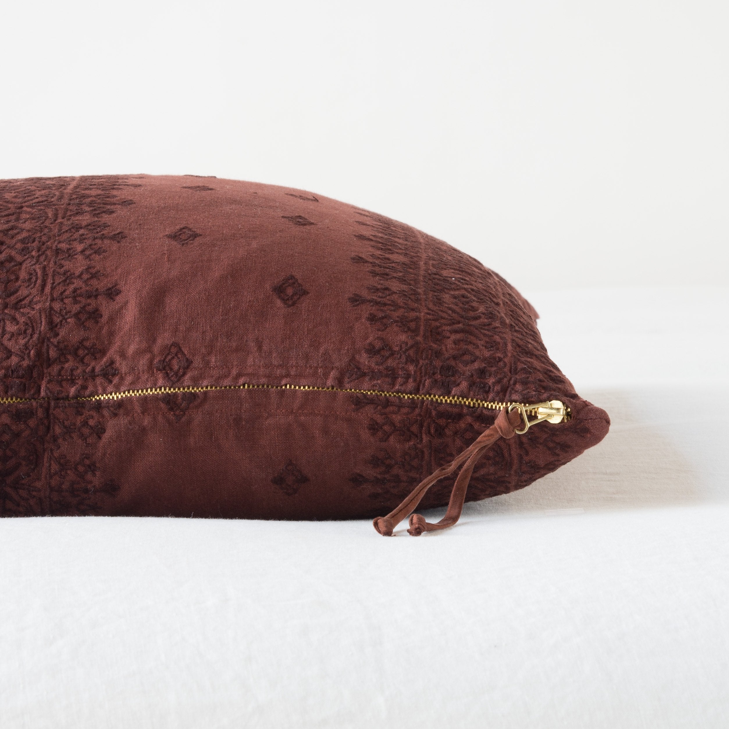 Mahogany: Close-up of brass zipper and charmeuse pull details on throw pillow - side view.