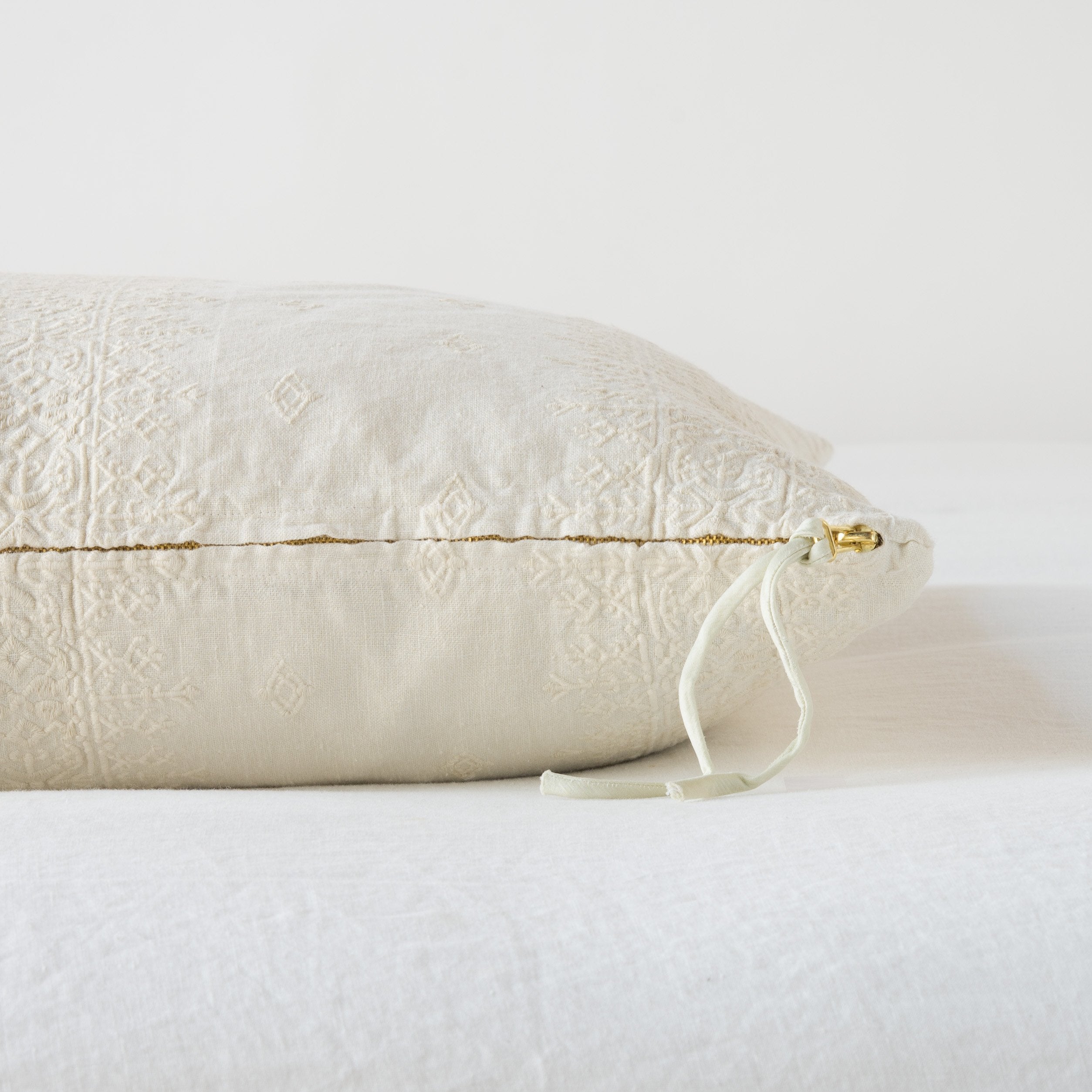 Parchment: Close-up of brass zipper and charmeuse pull details on throw pillow - side view.
