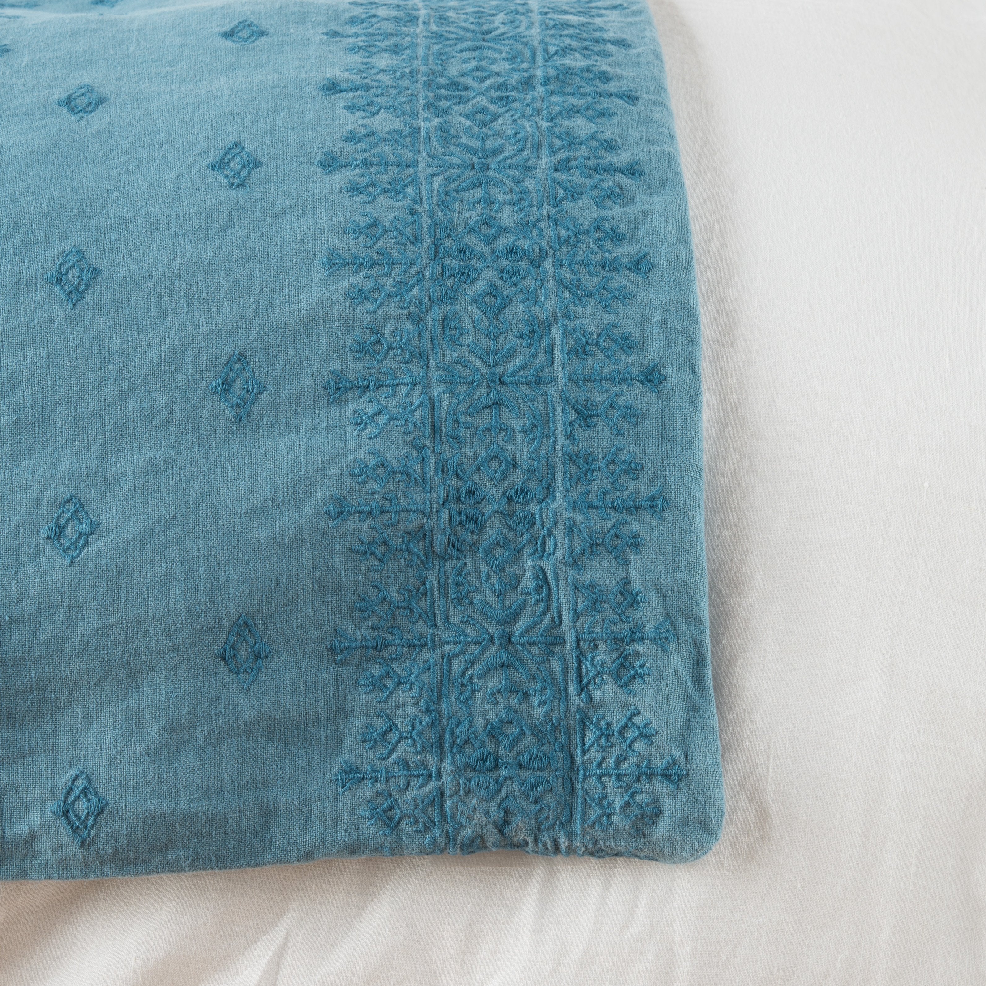 Cenote: Close-up of corner against a white background, showcasing embroidery pattern detail - overhead view.