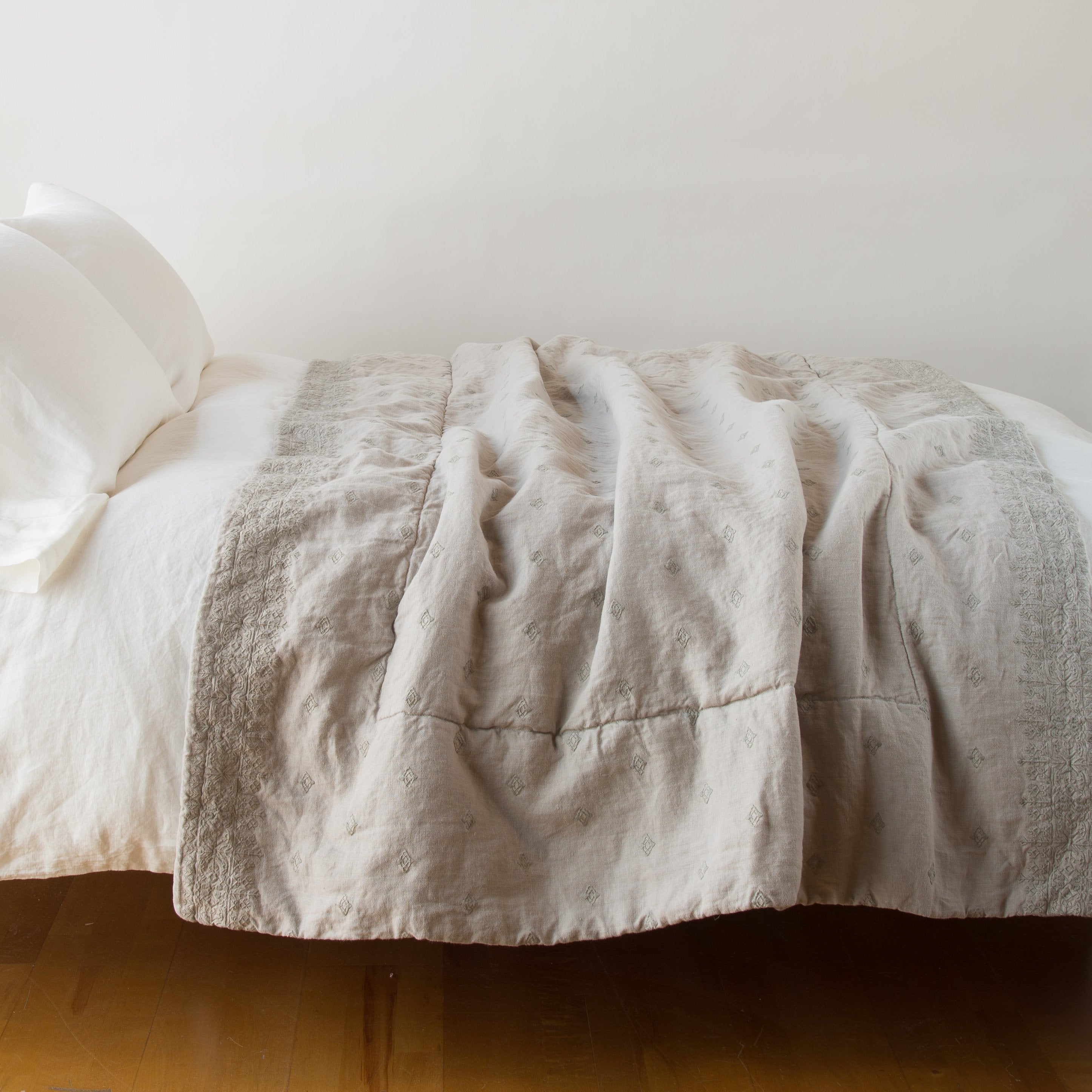 Fog: Ines embroidered midweight linen throw blanket, draped over a simple white bed - side view.