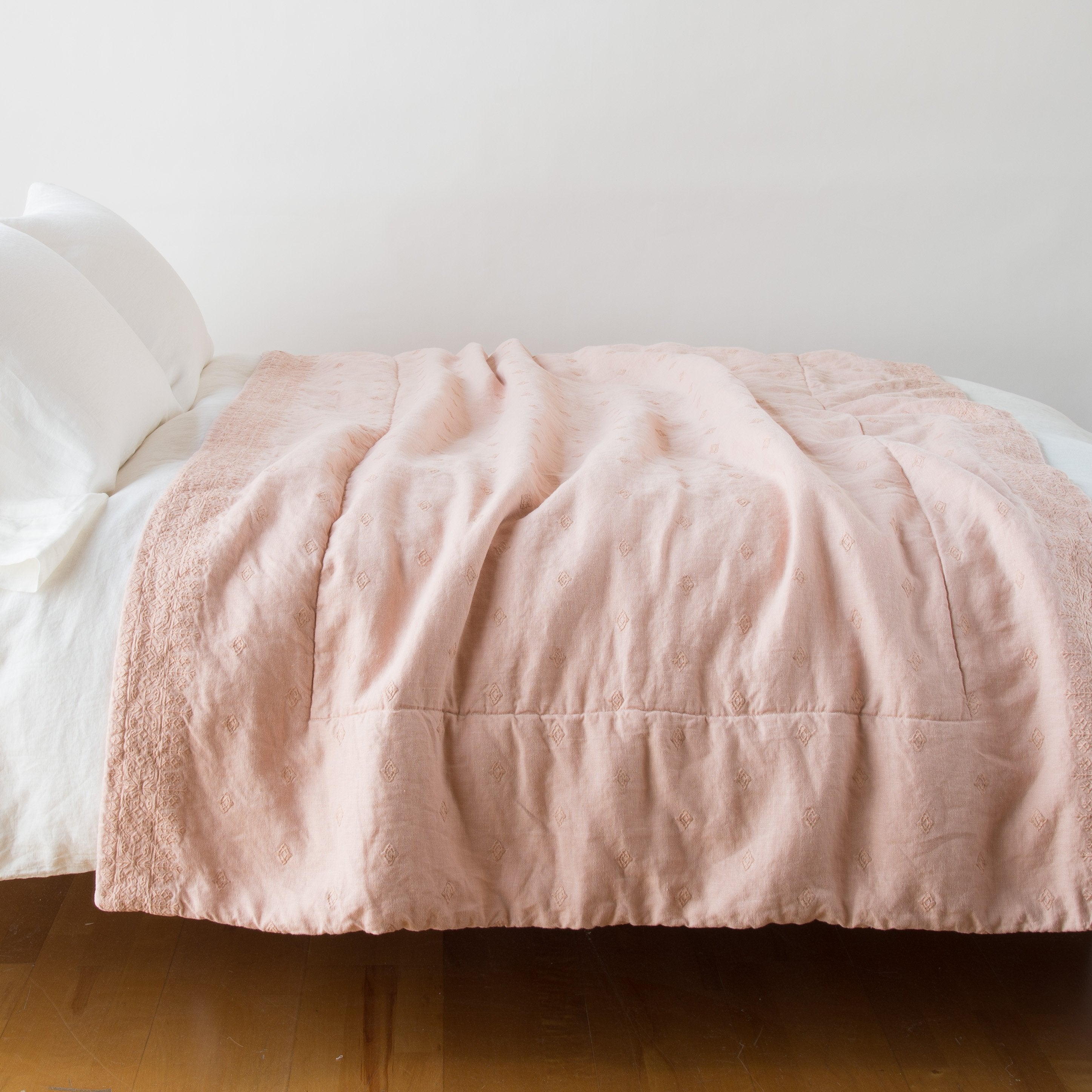 Rouge: Ines throw blanket in rouge, draped over a simple white bed - side view.