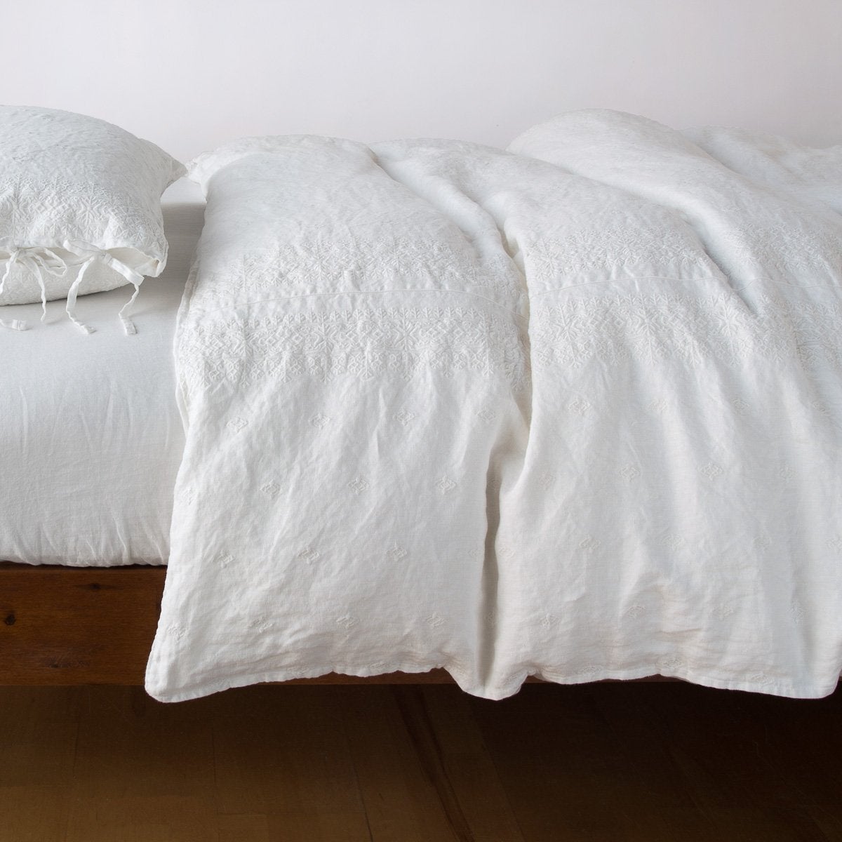 : Ines duvet cover in winter white, lightly rumpled on a monochromatic bed against a plain background - side view.