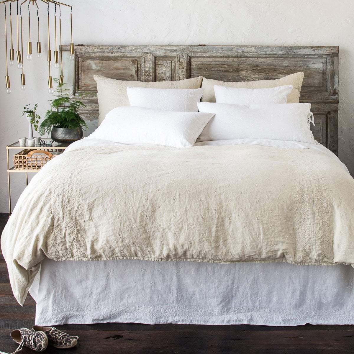 : Ines duvet cover, shams and bed skirt in parchemnt and white, against a distressed wood headboard and brass room accents - end of bed view.