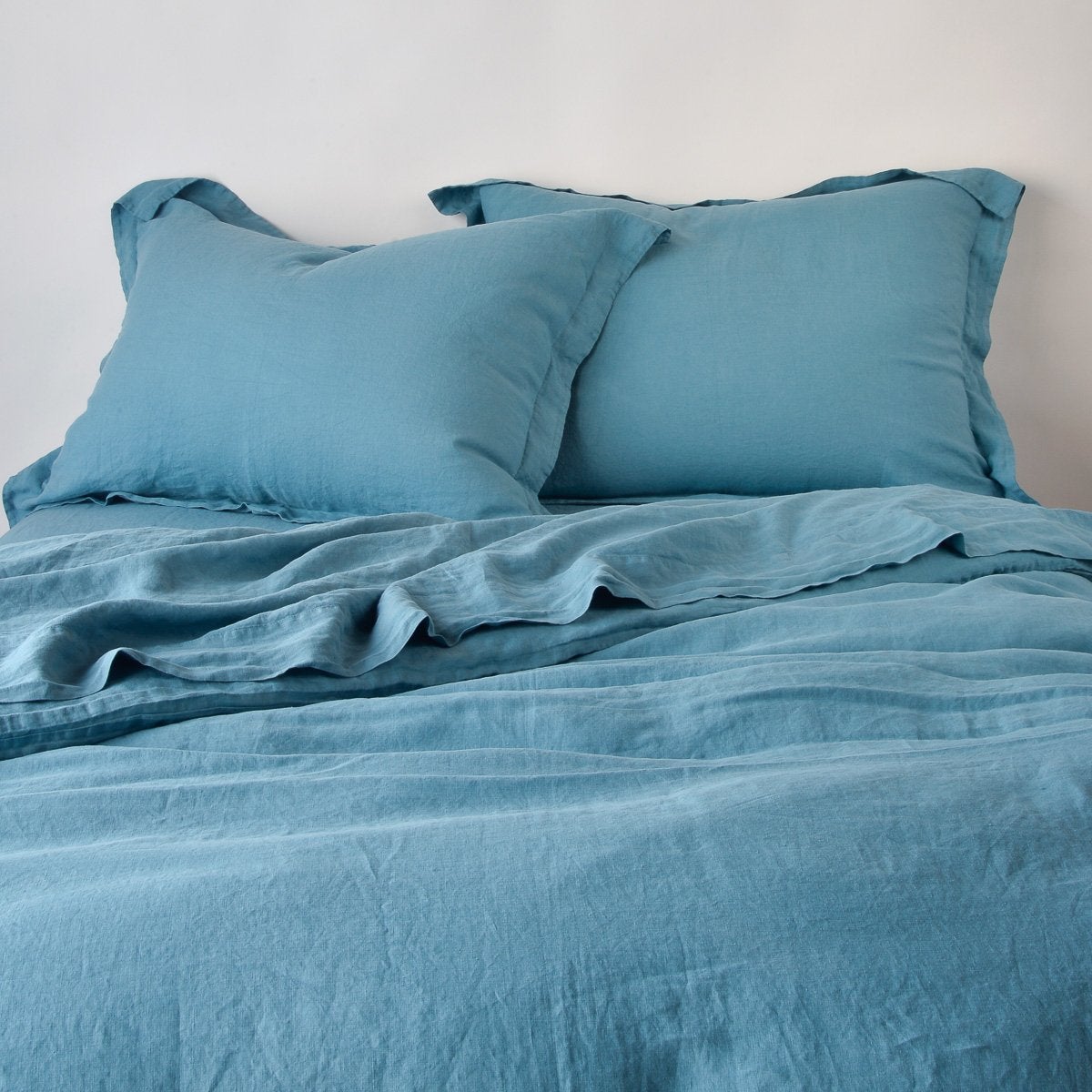 Cenote: duvet cover partially folded back on a bed with matching sheets and shams against a white wall - cropped end of bed view.