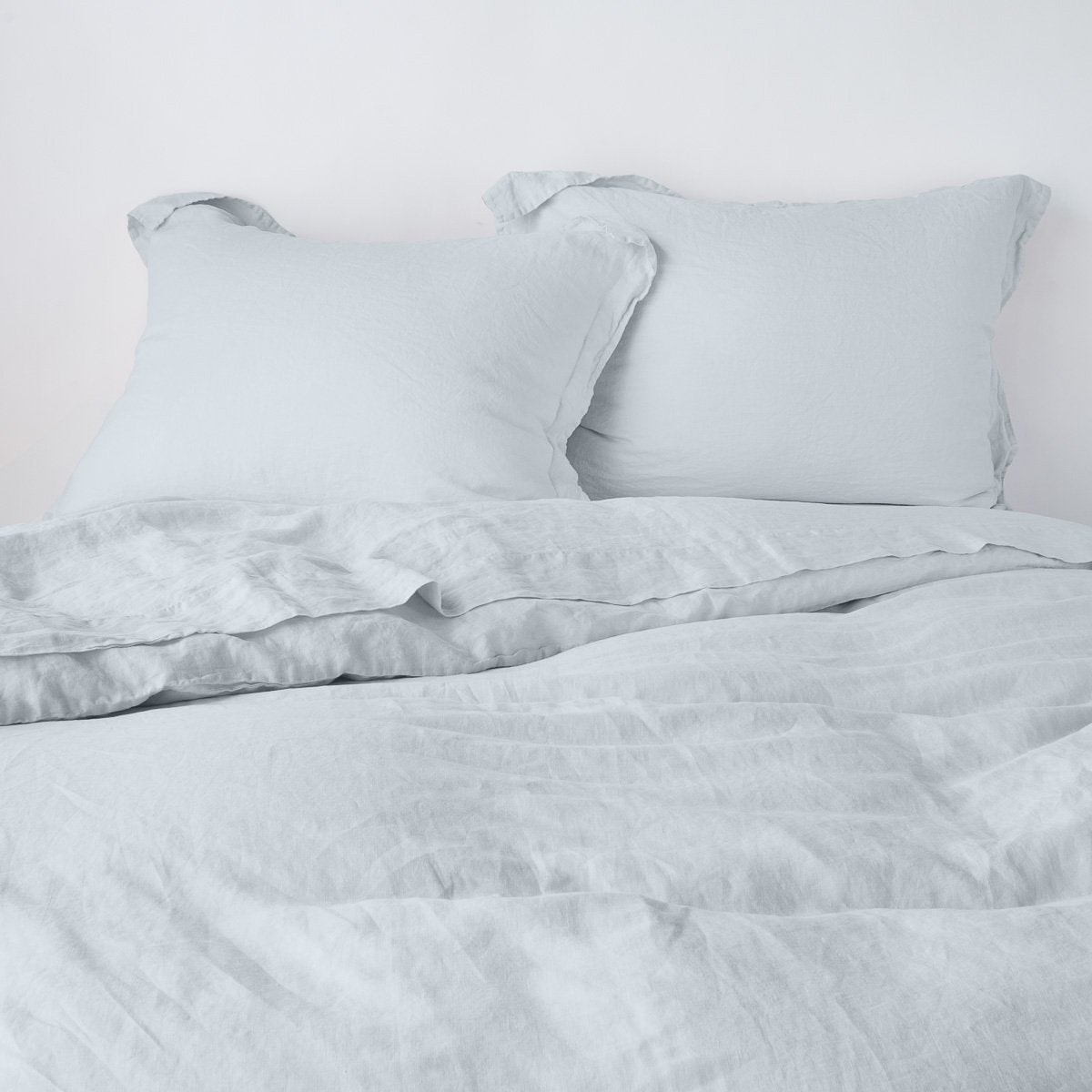 Cloud: duvet cover partially folded back on a bed with matching sheets and shams against a white wall - cropped end of bed view.