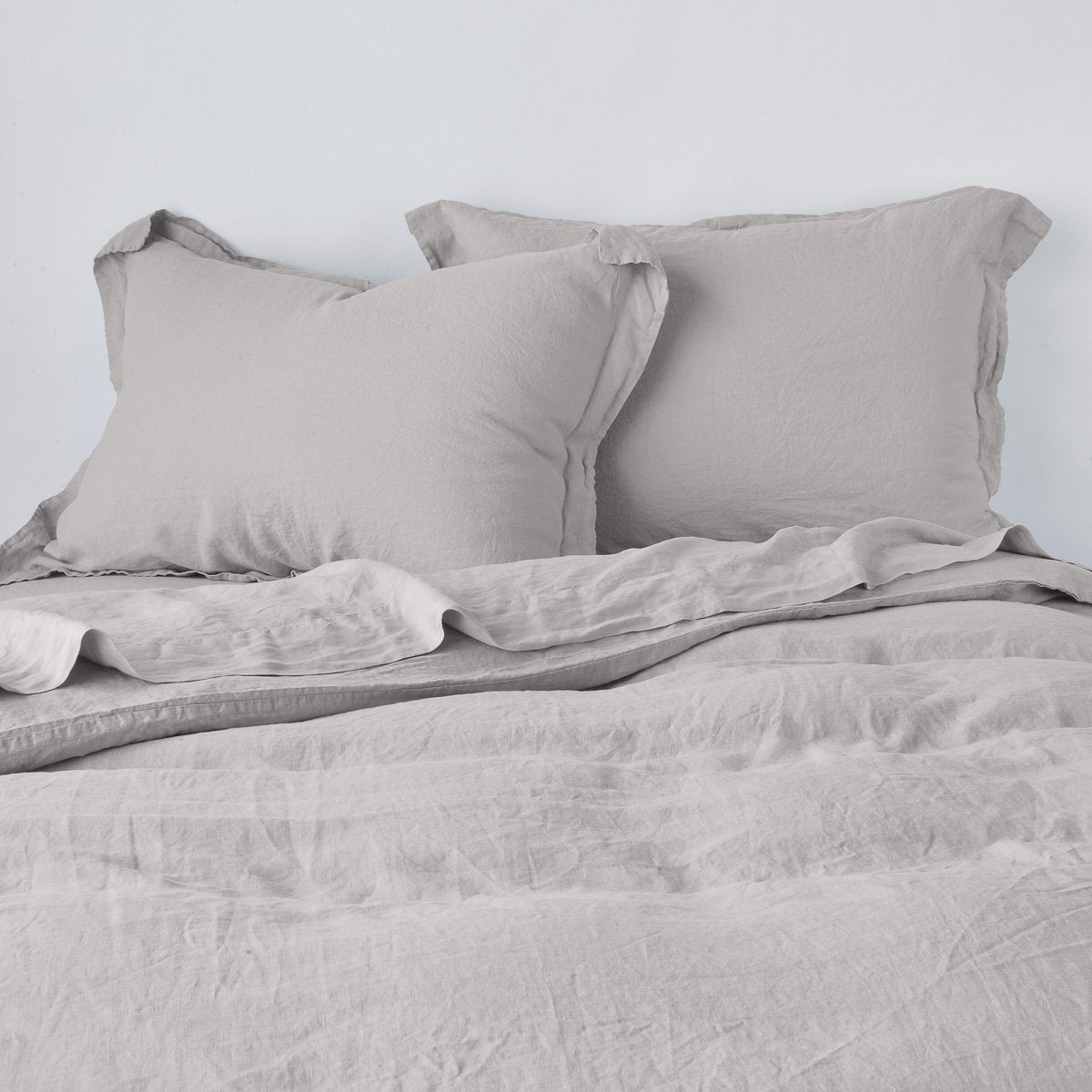 Fog: duvet cover partially folded back on a bed with matching sheets and shams against a white wall - cropped end of bed view.