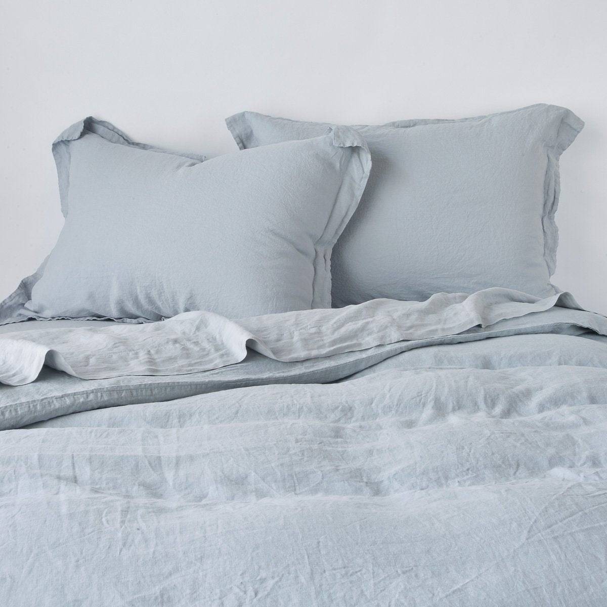 Mineral: duvet cover partially folded back on a bed with matching sheets and shams against a white wall - cropped end of bed view.