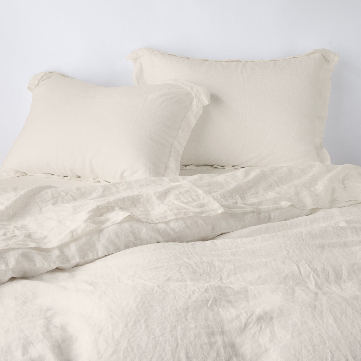 Parchment: duvet cover partially folded back on a bed with matching sheets and shams against a white wall - cropped end of bed view.