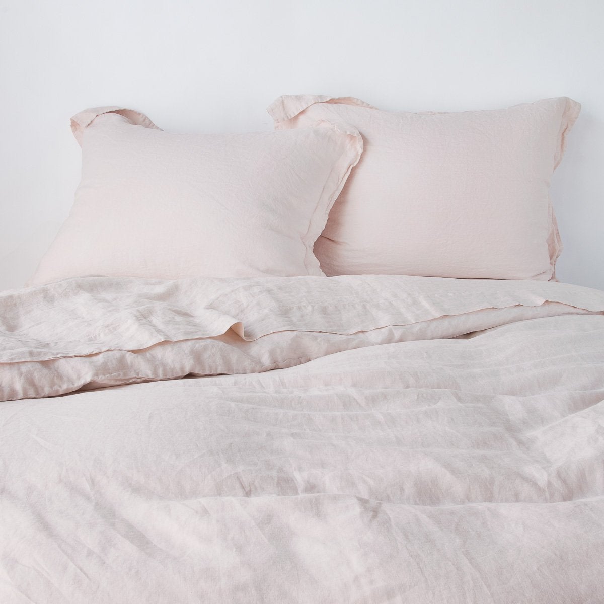 Pearl: duvet cover partially folded back on a bed with matching sheets and shams against a white wall - cropped end of bed view.