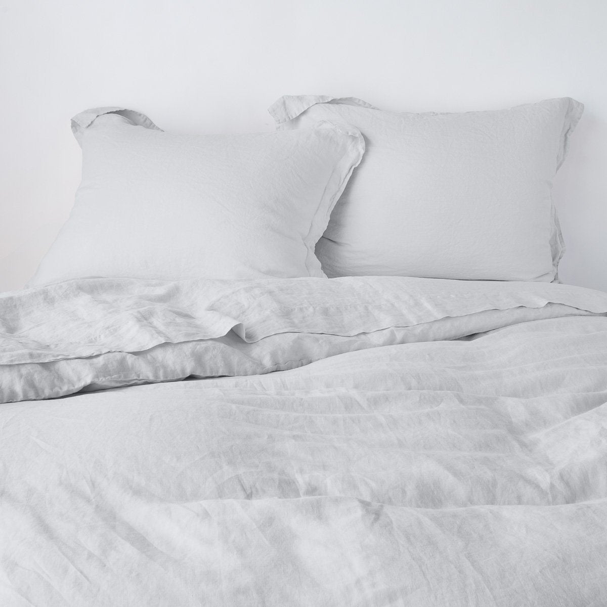 Sterling: duvet cover partially folded back on a bed with matching sheets and shams against a white wall - cropped end of bed view.