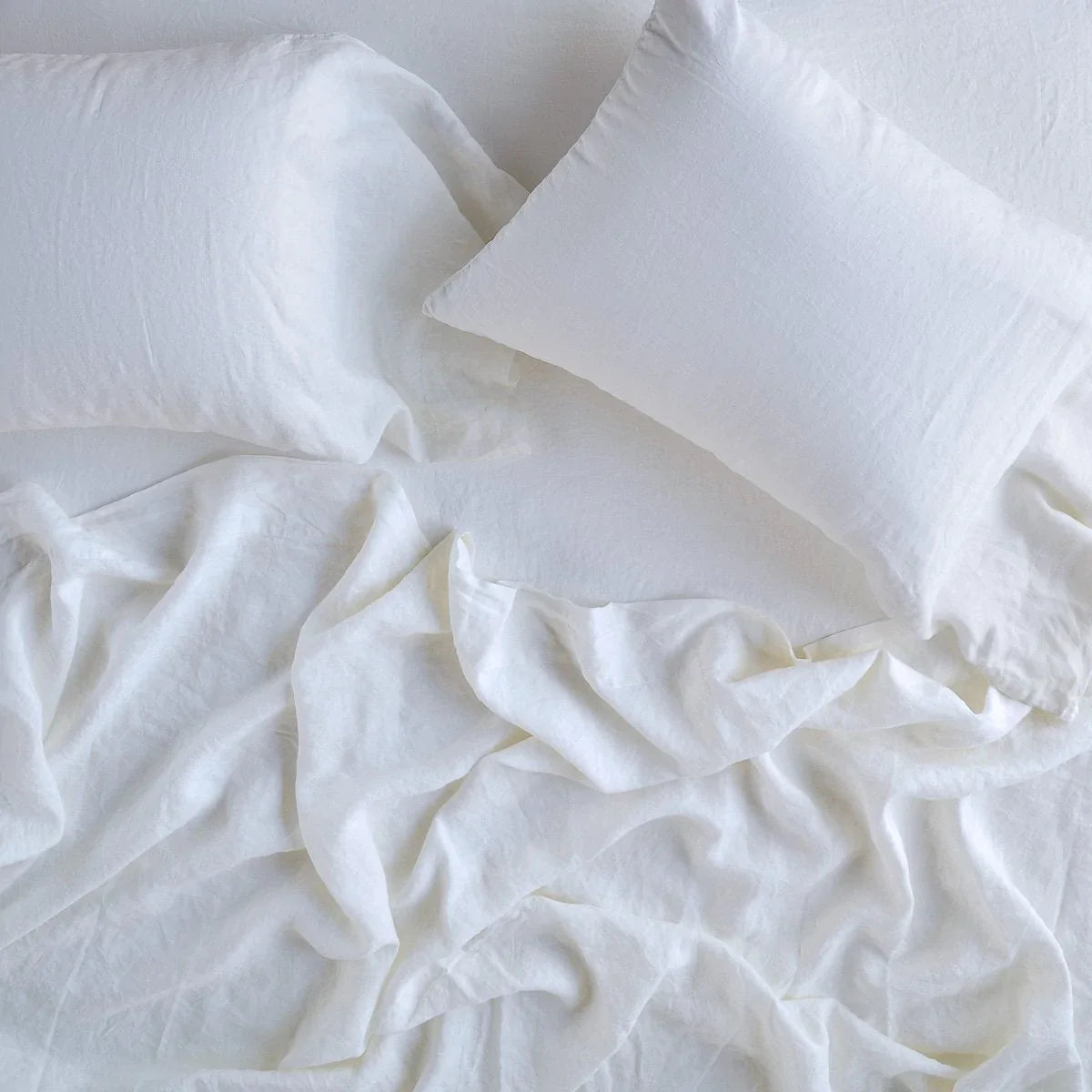 White: fitted sheet with matching rumpled flat sheet and sleeping pillows - overhead view.