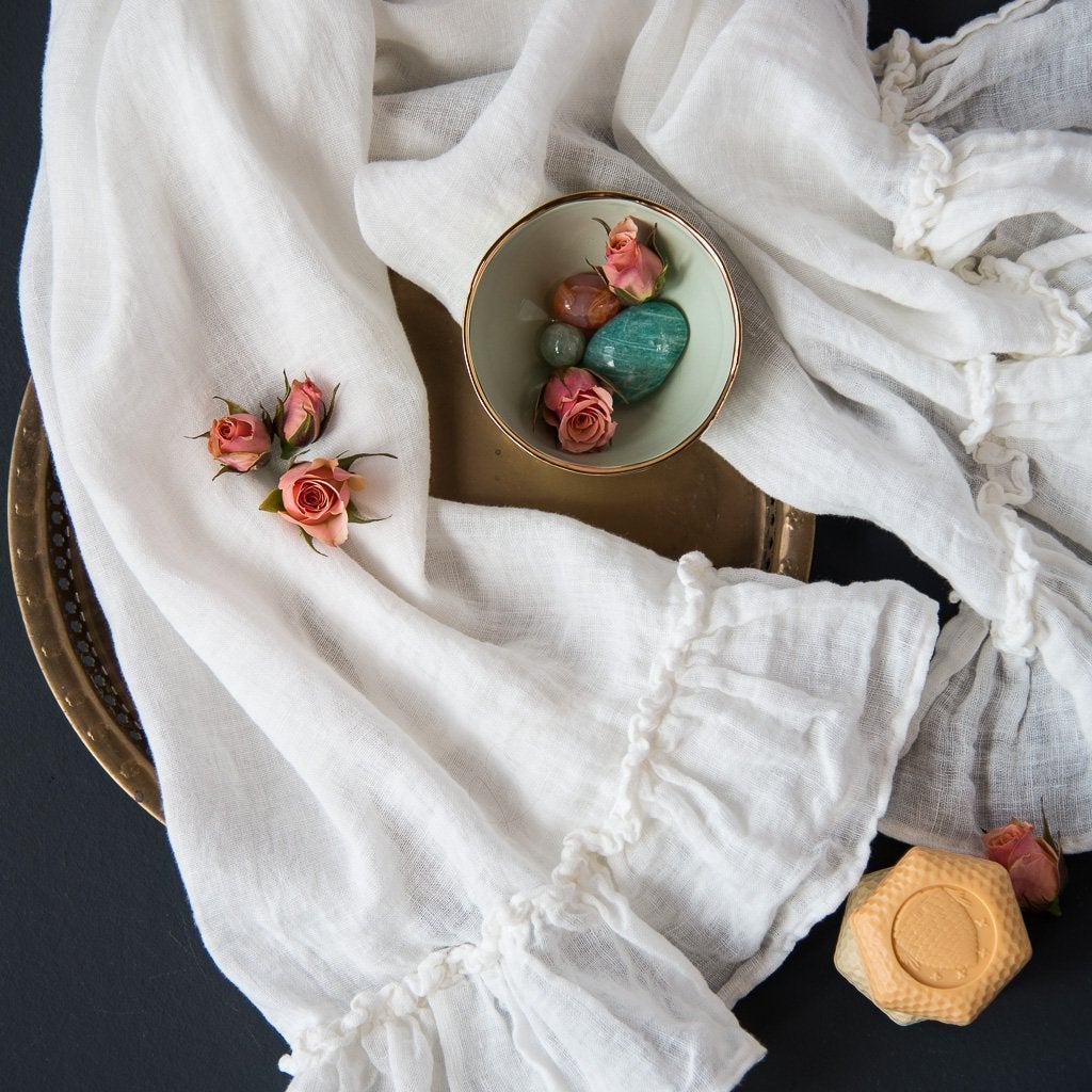 : Linen Whisper guest towel in winter white, draped over a dark background and tray with soft coral and green accessories - overhead view.