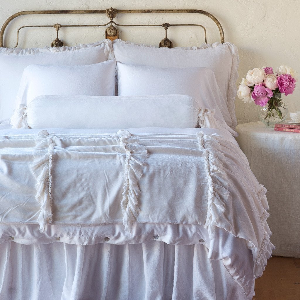 : Loulah shams on a neatly made all-white bed with matching bolster and throw blanket - end of bed view.