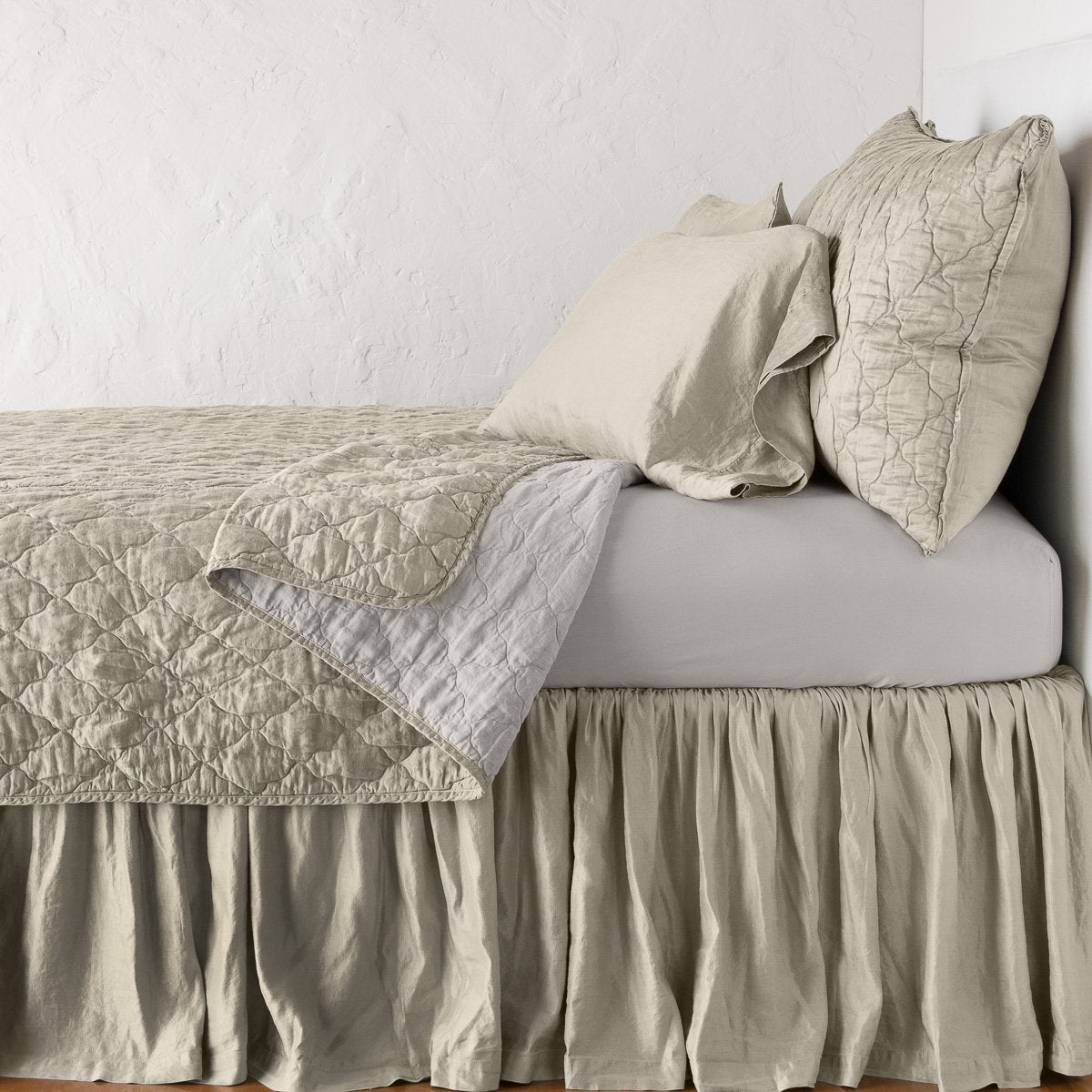 Fog: coverlet neatly folded back to reveal linen reverse, on a monochromatic bed - side view.