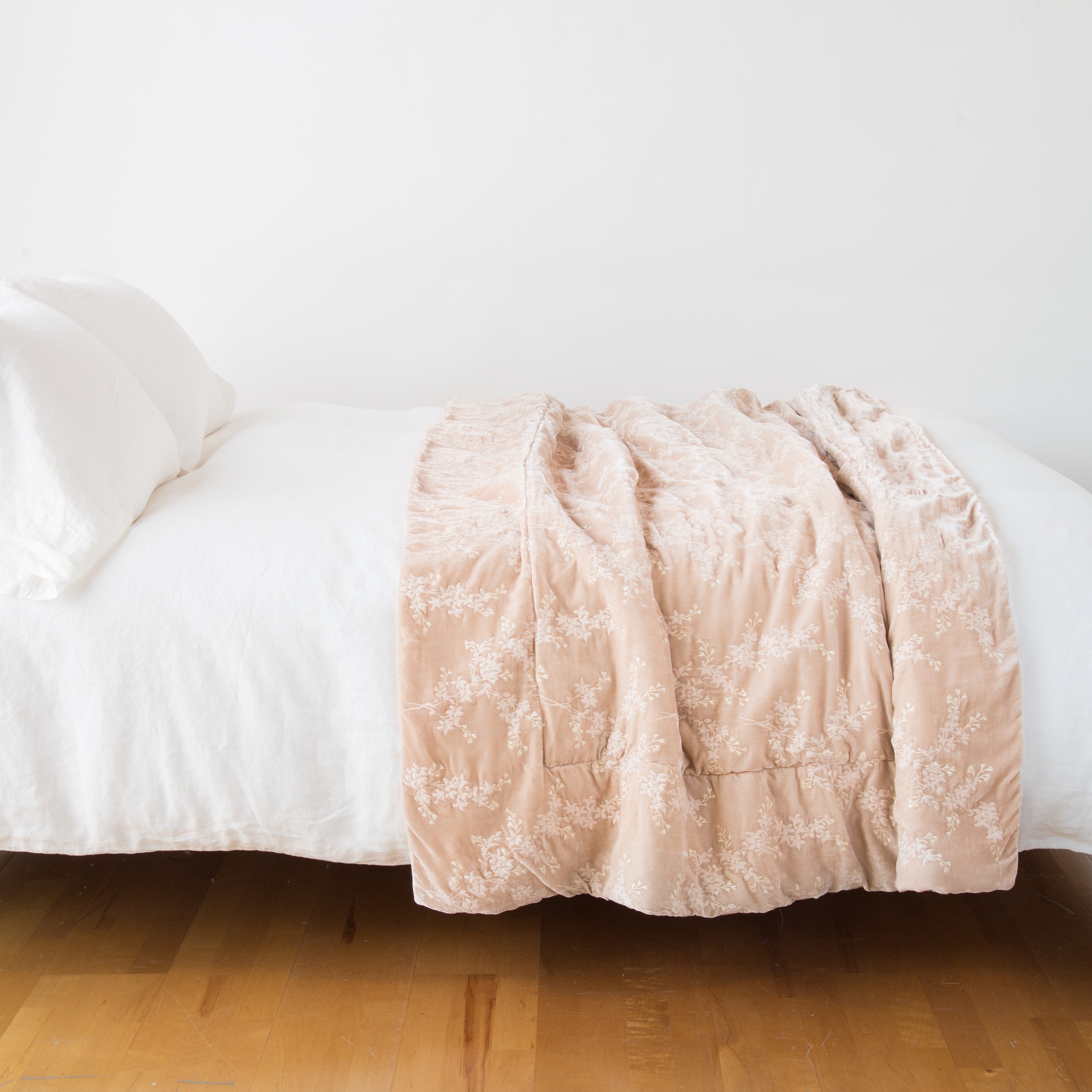 : Lynette throw blanket in pearl, draped over a simple white bed - side view.