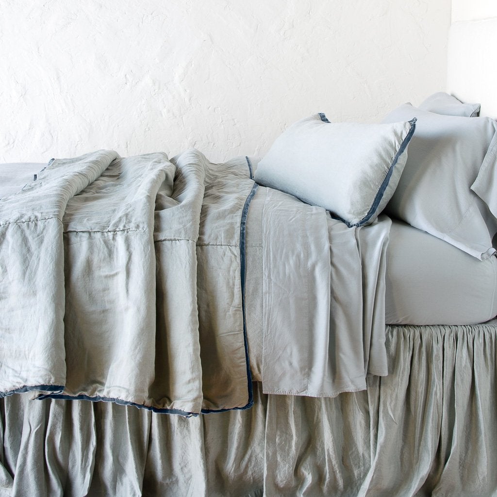 Mineral: throw blanket rumpled on a charmeuse monochromatic bed - side view.