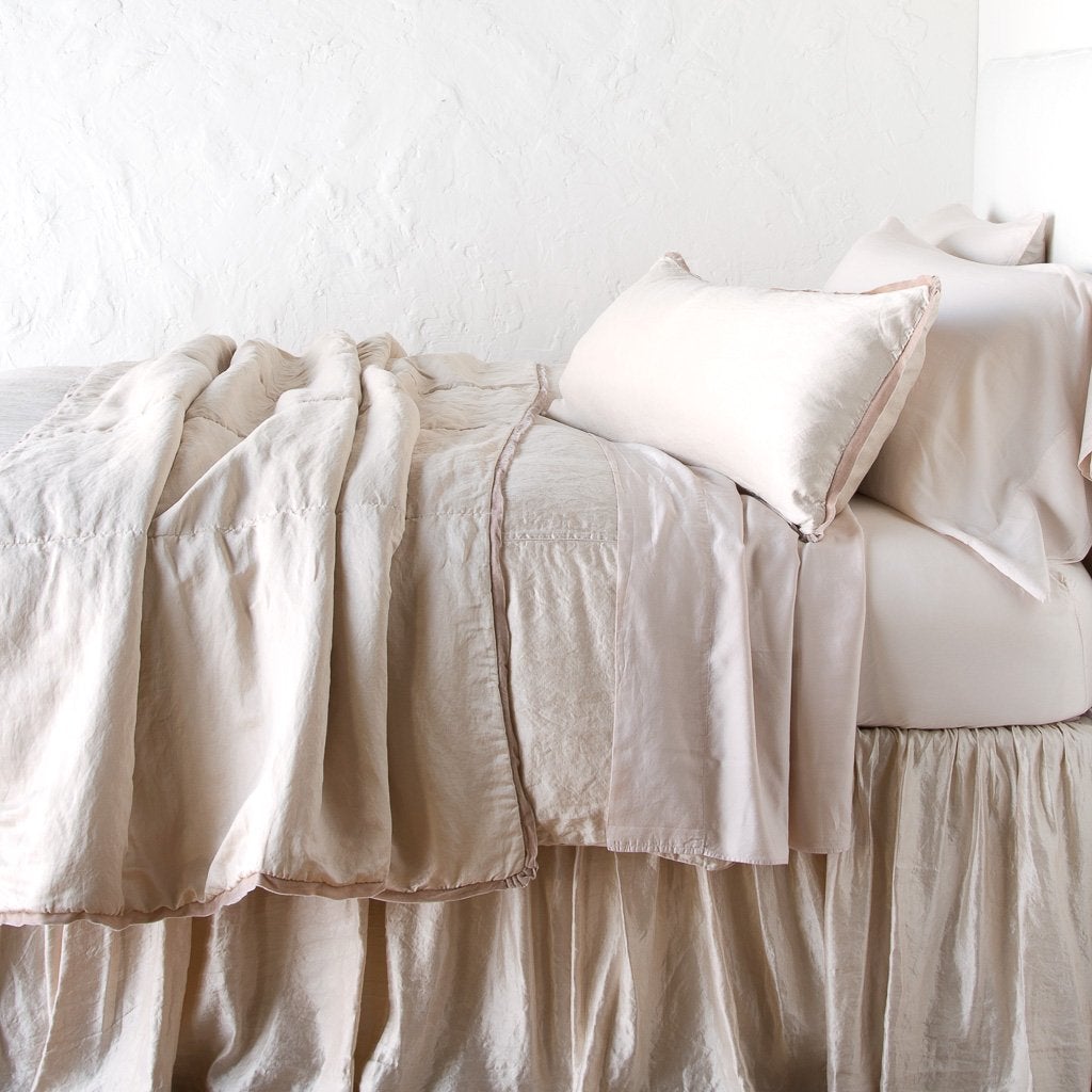 : Paloma throw blanket rumpled on a charmeuse monochromatic bed - pearl, side view.