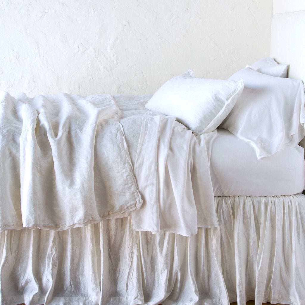 White: throw blanket rumpled on a charmeuse monochromatic bed - side view.