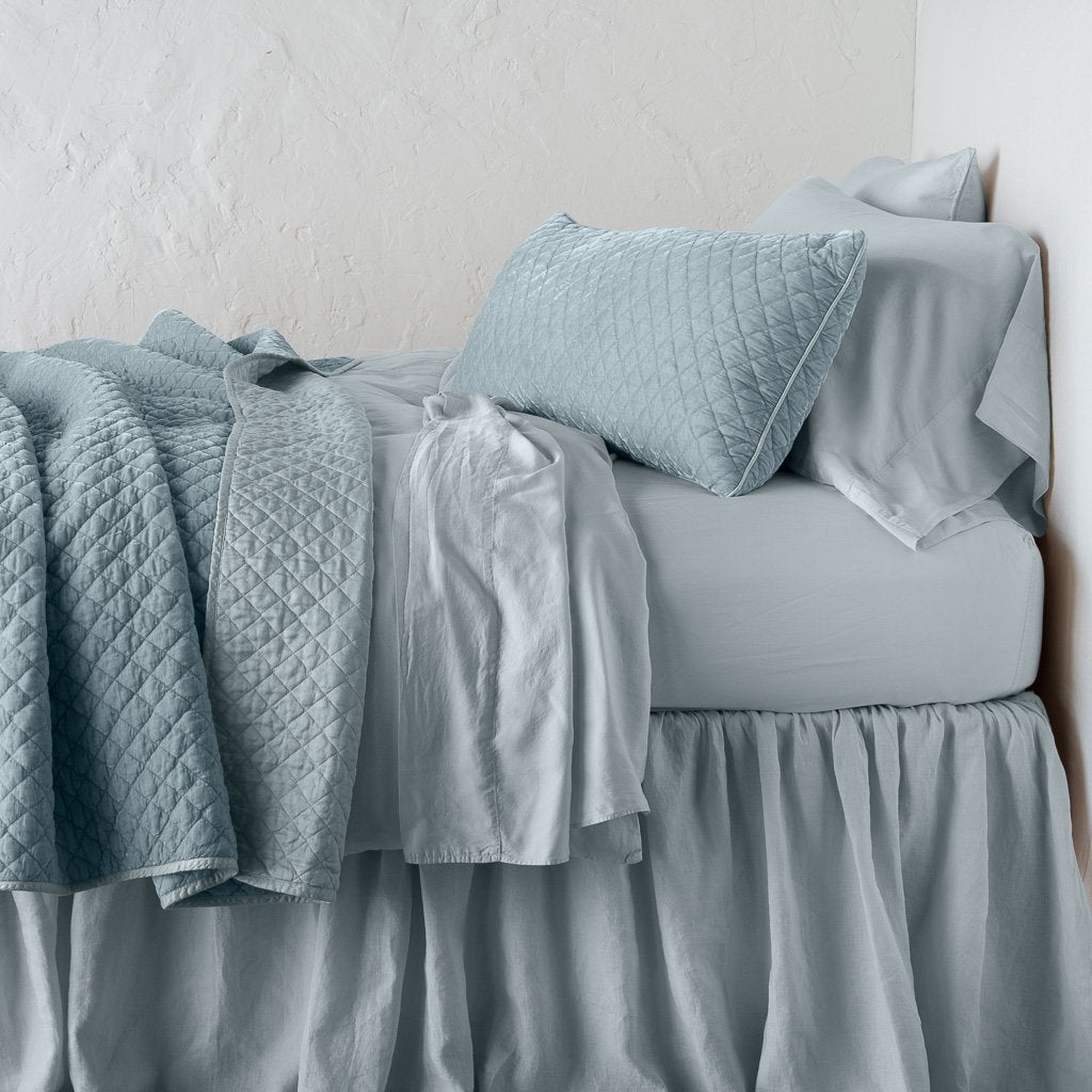 Cloud: throw blanket rumpled and folded back, featuring satin back. Shown with matching lumbar pillow and monochromatic sheeting - side view.