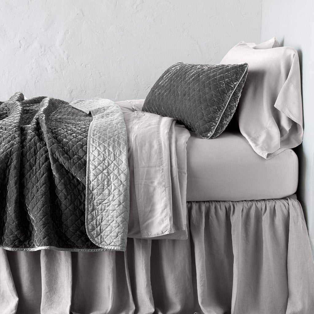 Fog: throw blanket rumpled and folded back, featuring satin back. Shown with matching lumbar pillow and monochromatic sheeting - side view.
