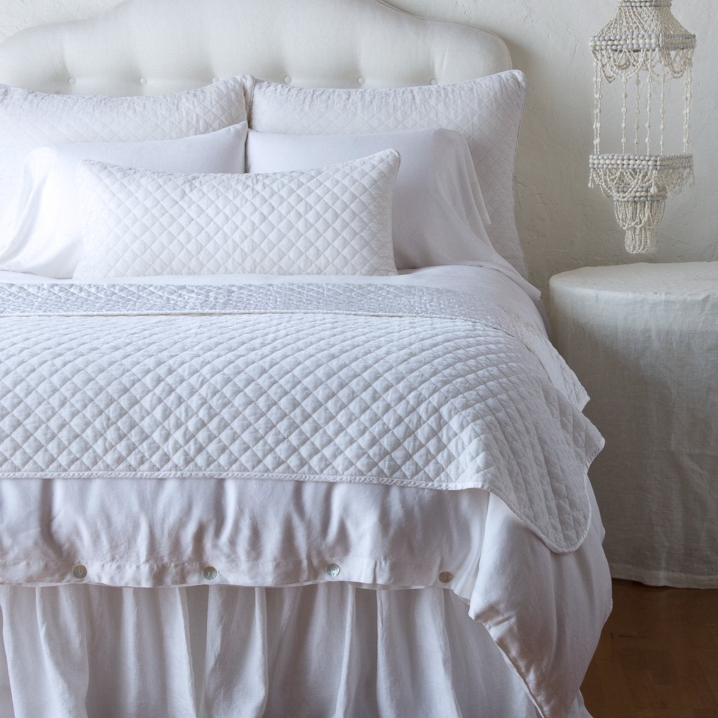 White: throw blanket and matching lumbar pillow on a neatly made white bed - end of bed view.