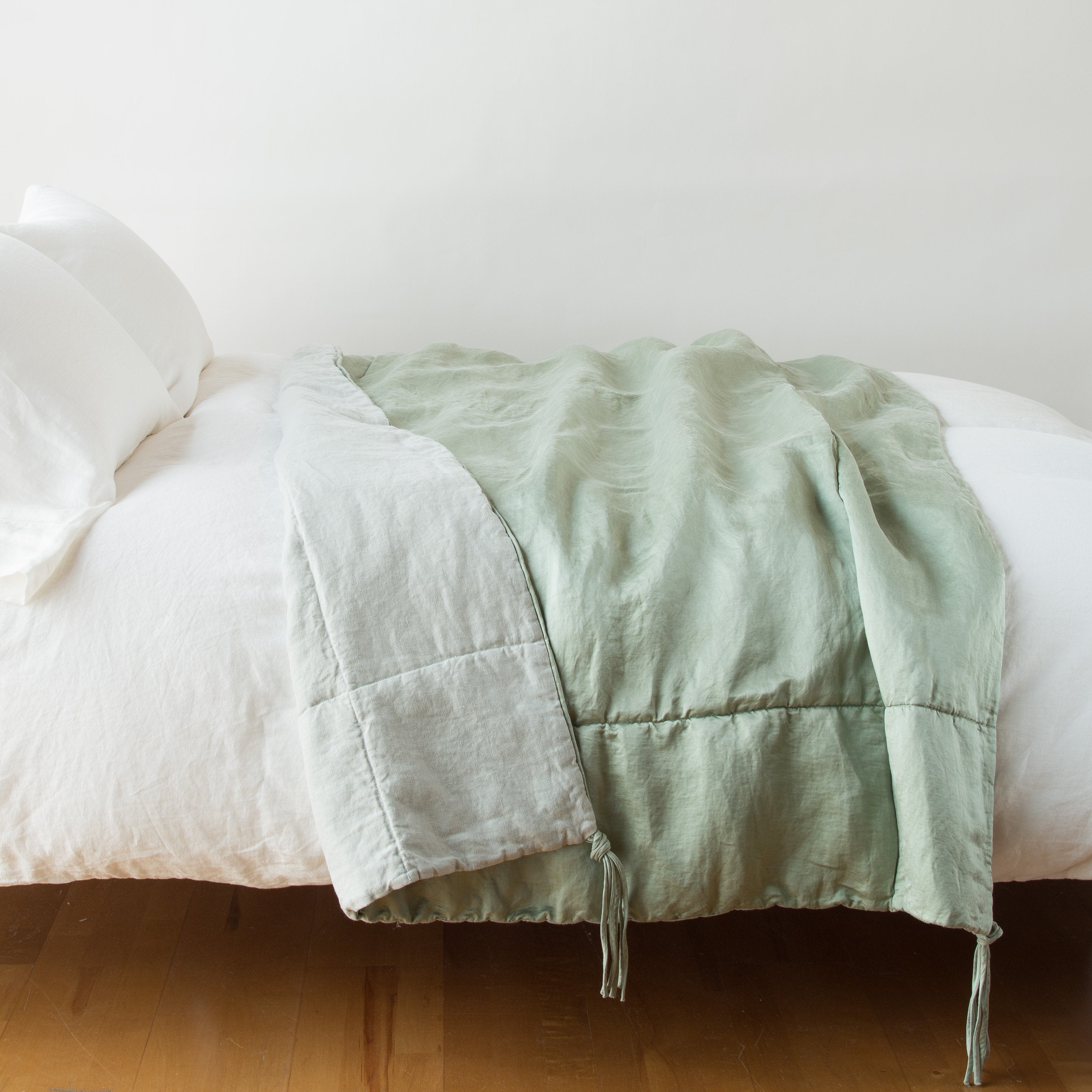 Eucalyptus: blanket draped over a white bed, folded back to reveal midweight linen back - side view.