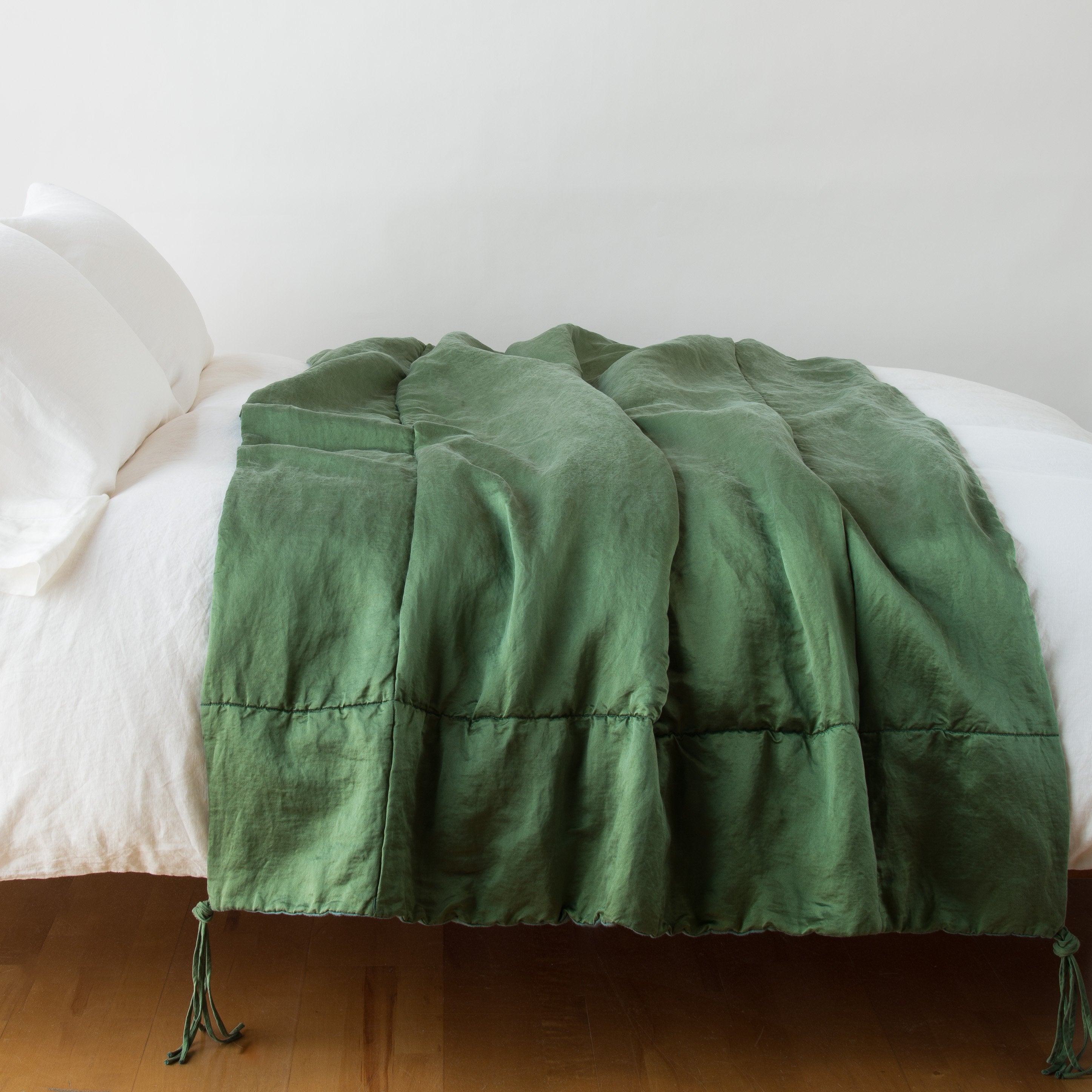 Jade: blanket draped over a white bed - side view.
