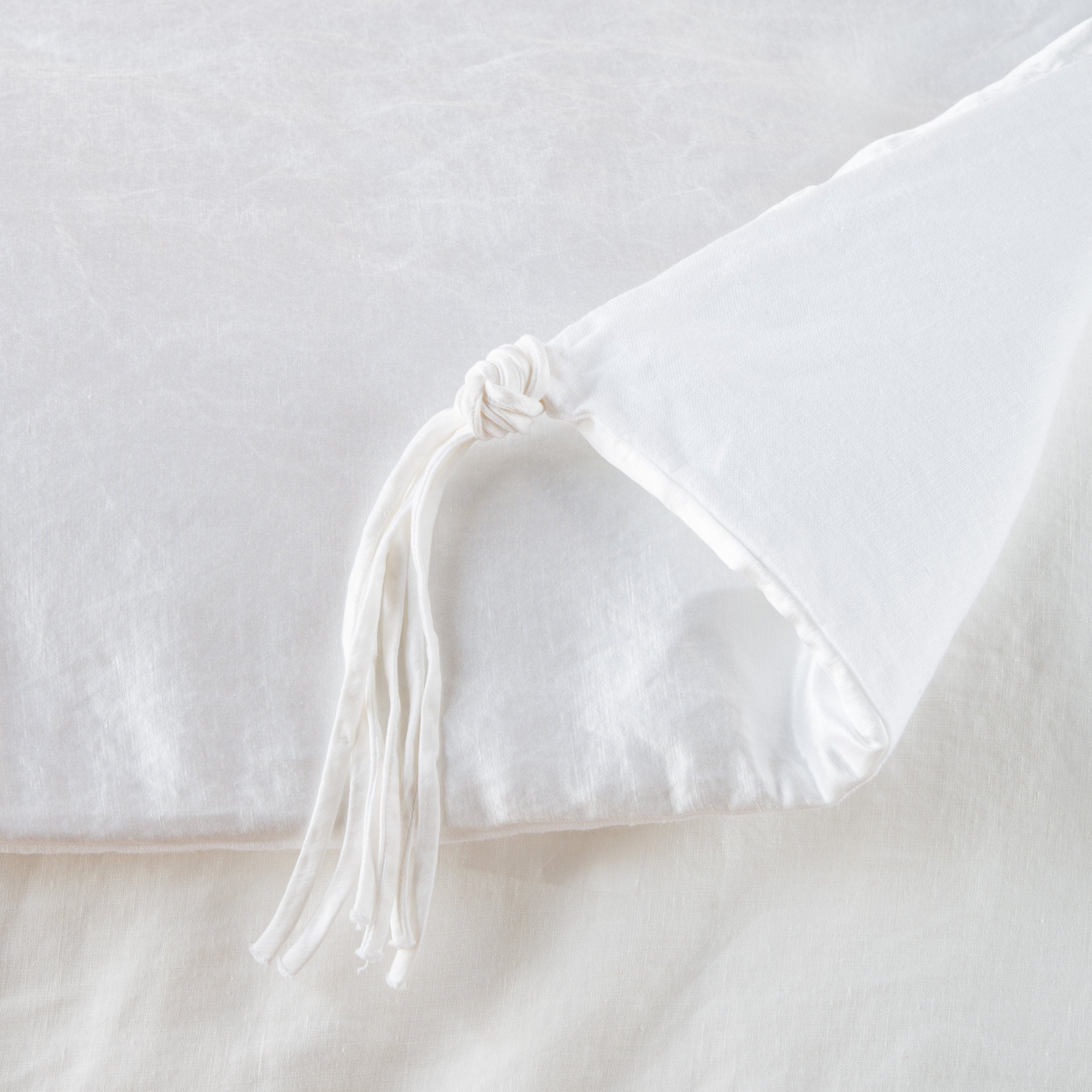 White: Close up of blanket, with a corner turned back to showcase the midweight linen back and corner tassel - overhead view.