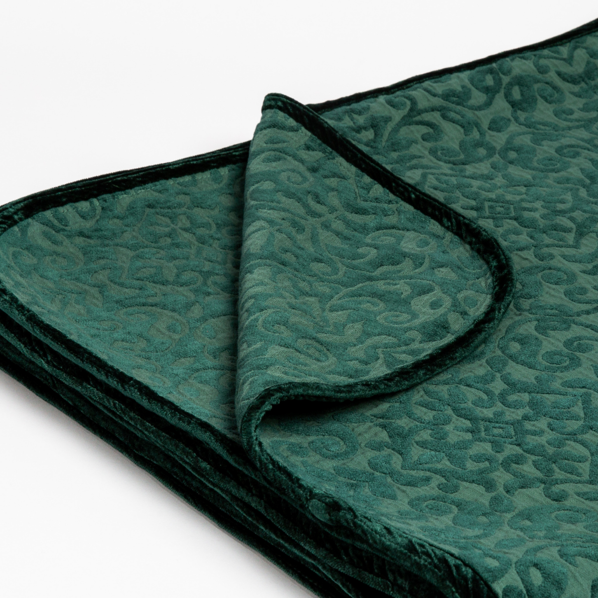 Jade: : Close up of the blanket folded with a corner pulled back to show the reverse and trim of the blanket. 