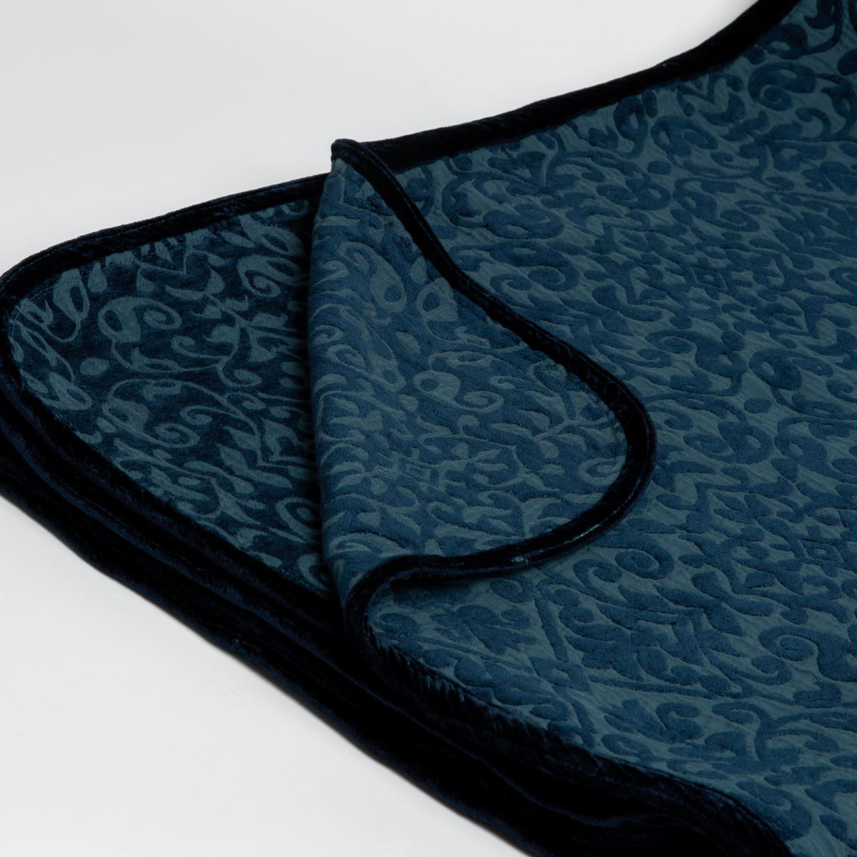 Midnight: : Close up of the blanket folded with a corner pulled back to show the reverse and trim of the blanket. 