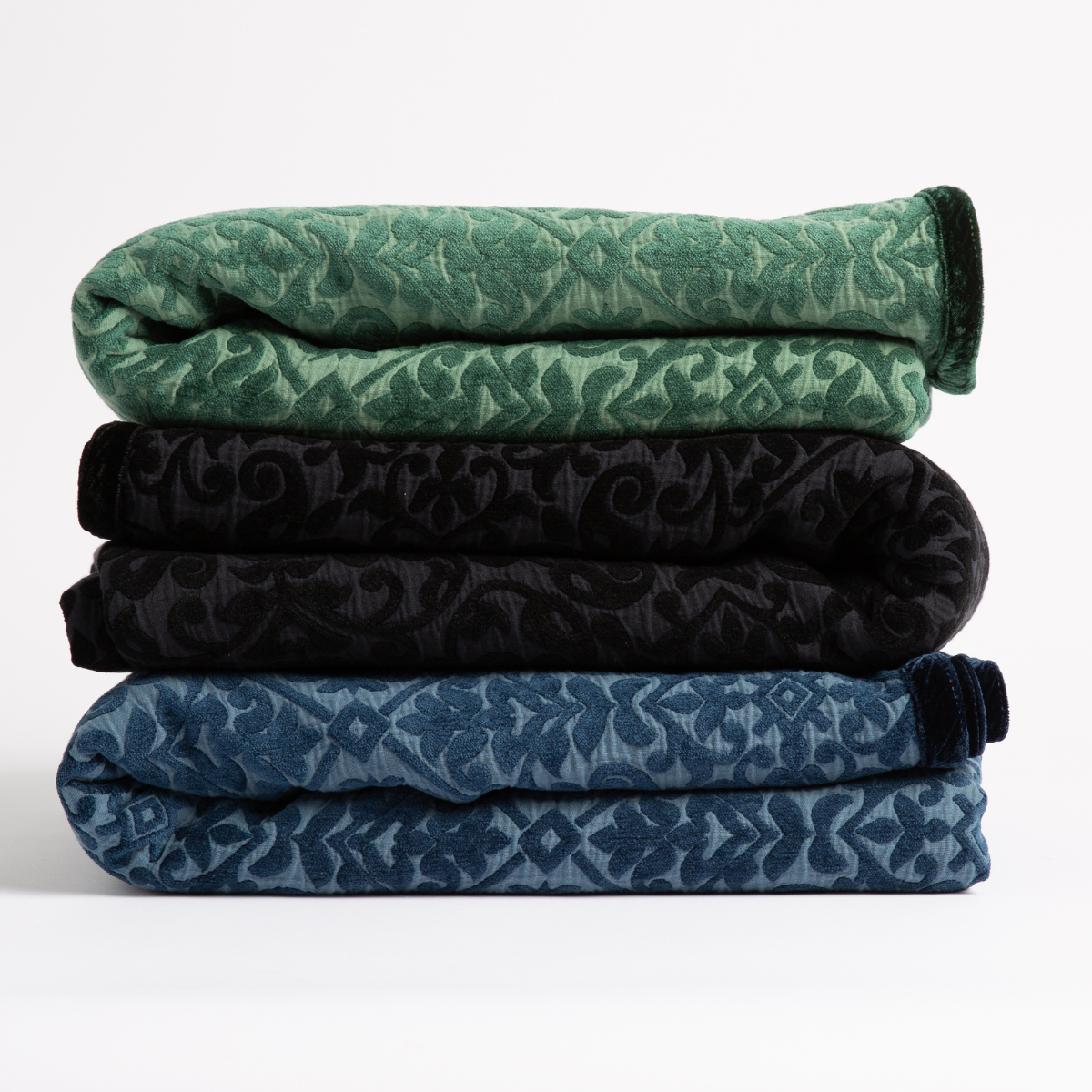 : three blankets in jade, corvino and midnight stacked against a white background.
