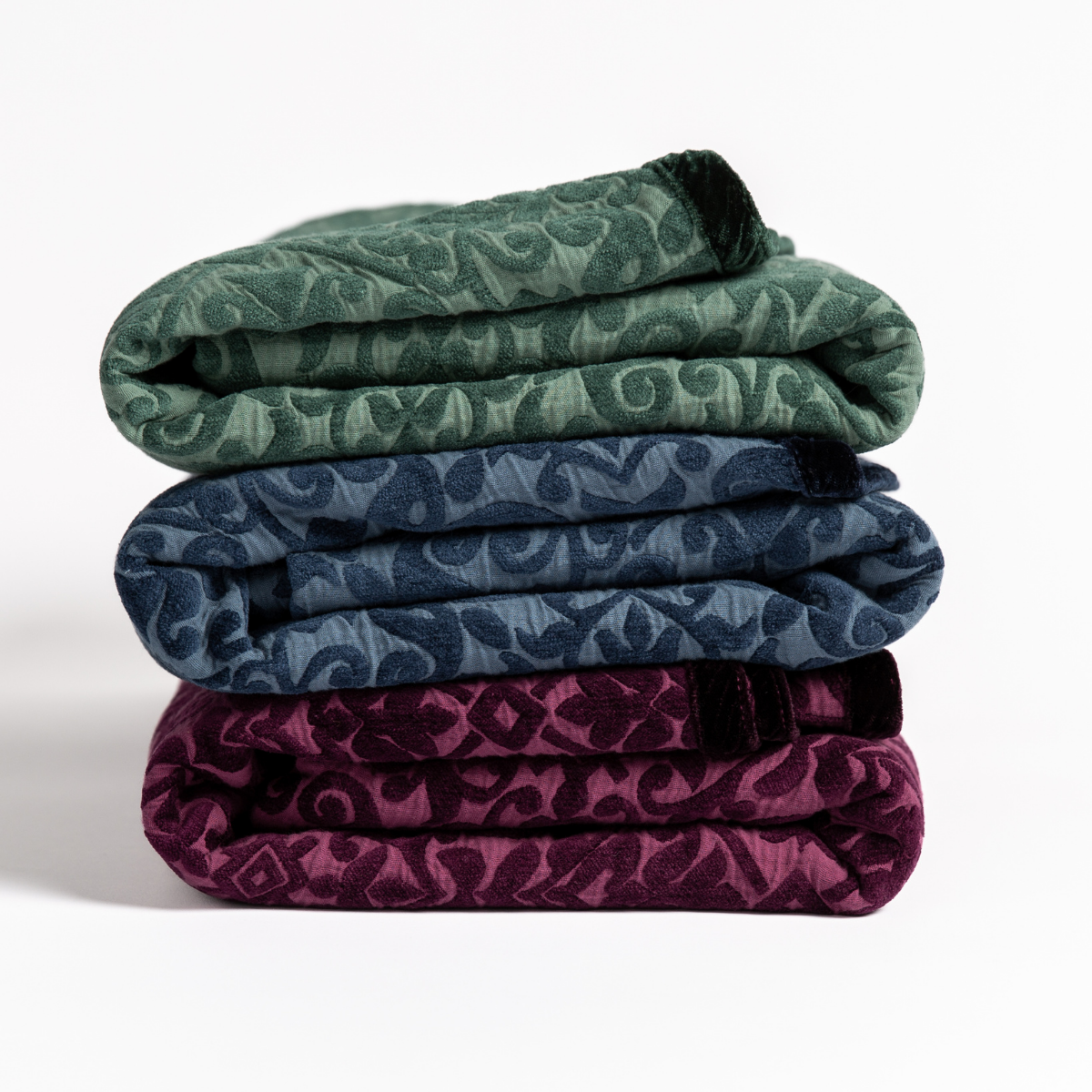 : Close up of folded blankets in Jade, Midnight and Fig against white background display the contrast of the pattern and trim. 